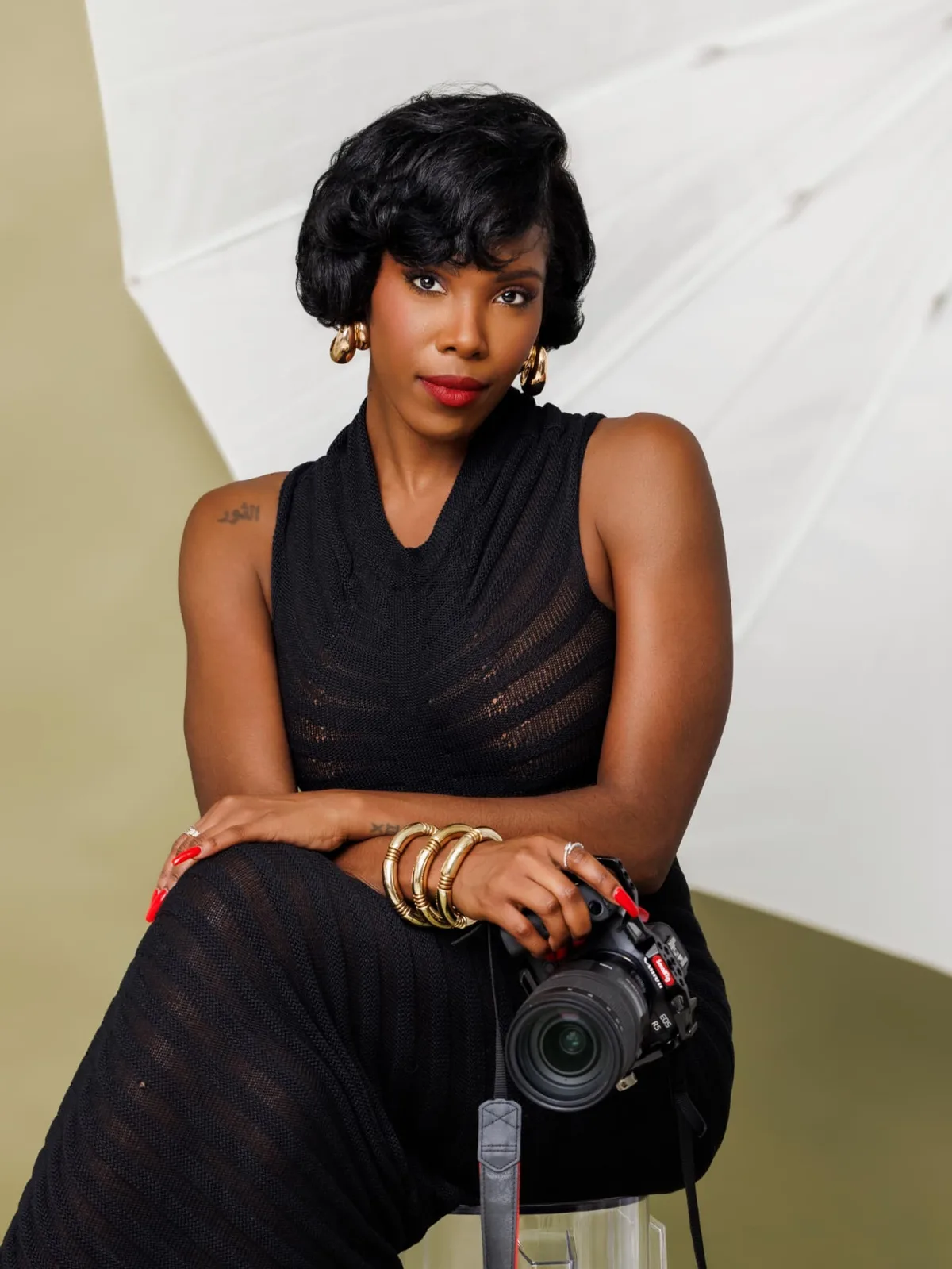 Jasmine “JLavii” Hutcherson seated in her studio holding her camera, softbox umbrella behind her